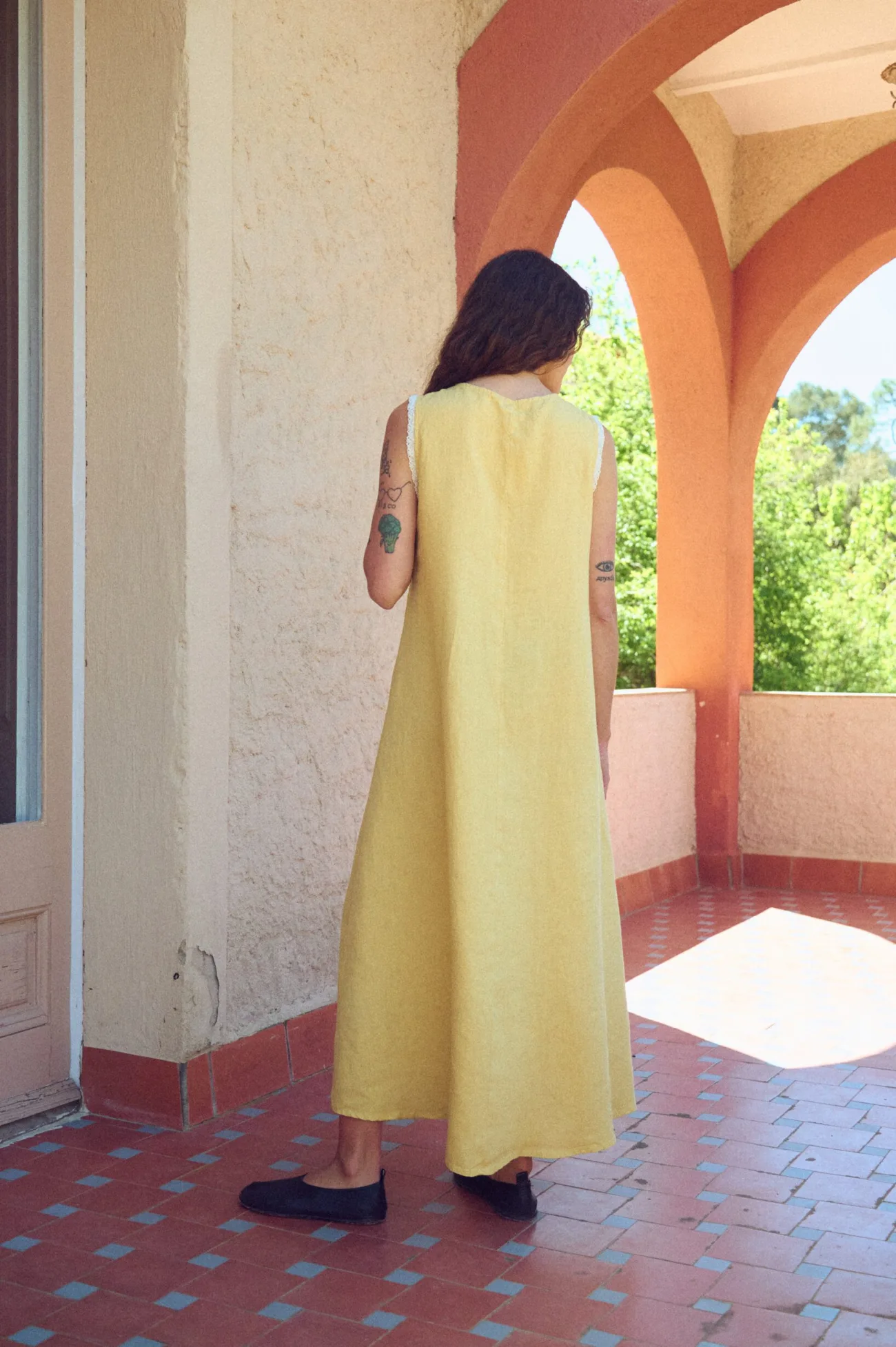 Back view of butter yellow linen sleeveless maxi dress with lace-trimmed armholes and a relaxed A-line drape