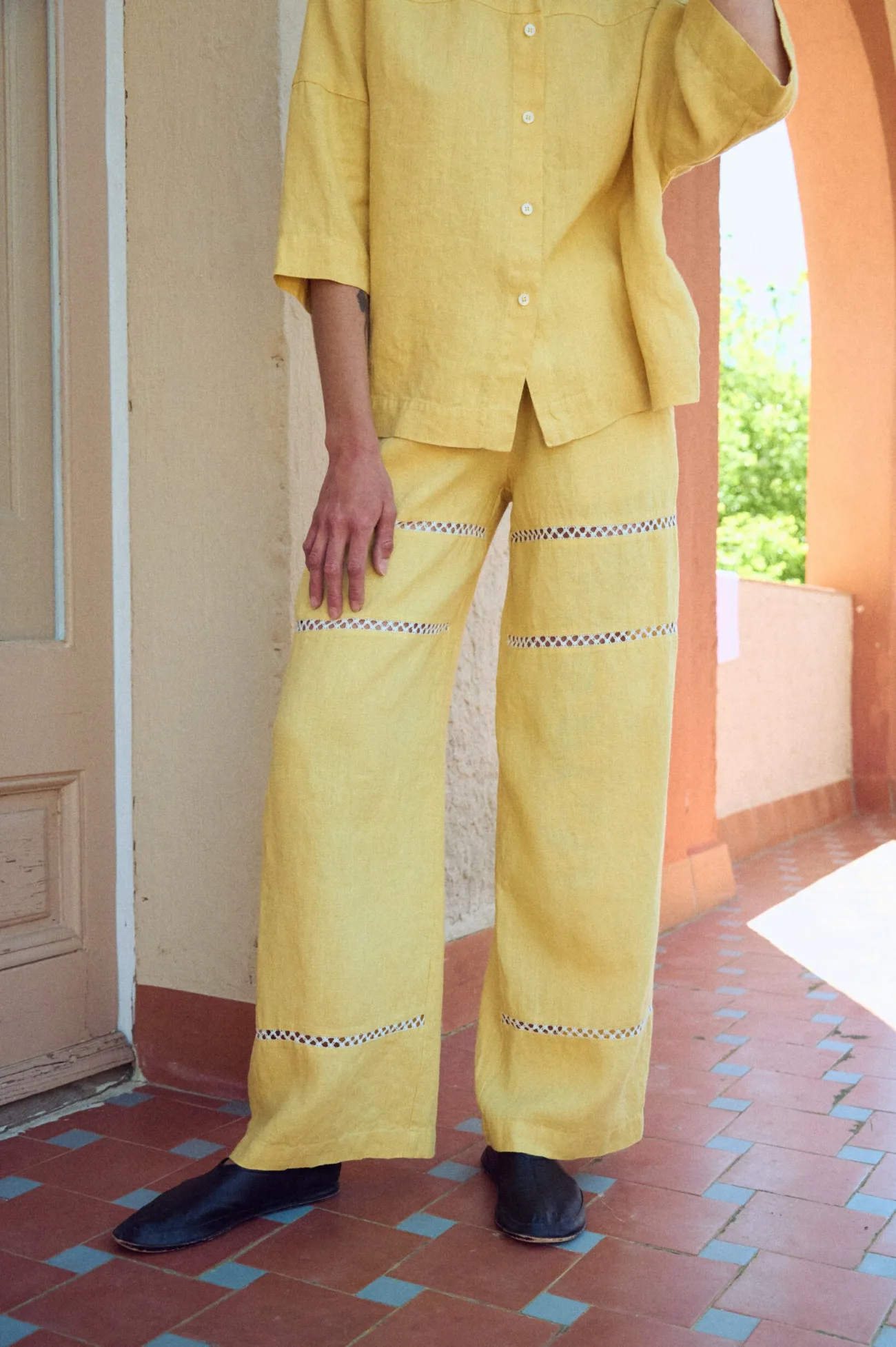 Soft yellow linen trousers with a relaxed, wide-leg fit and airy drape, featuring delicate openwork lace insert panels across the leg and a comfortable elastic waistband for ease of wear