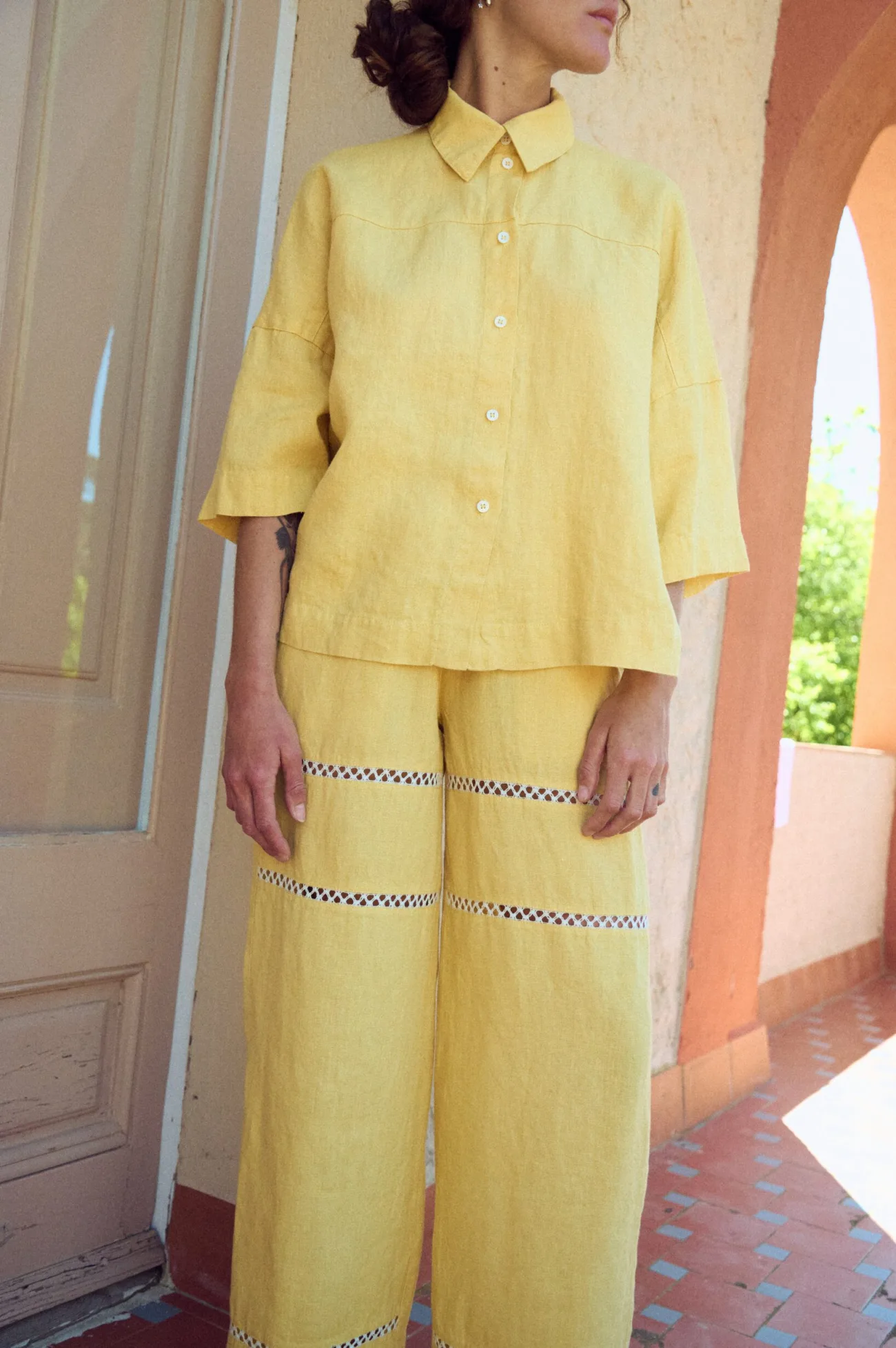 Wide-leg yellow linen pants with a relaxed, airy drape, featuring horizontal openwork lace insert panels along the legs and a comfortable elastic waistband for an easy fit, paired with a matching shirt