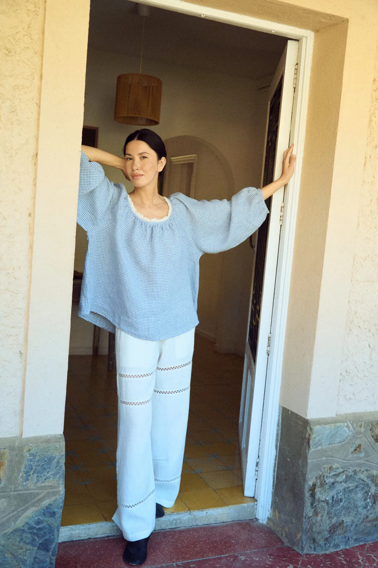 White linen trousers with a wide-leg silhouette and delicate horizontal lace insets, designed with a soft elastic waistband and an easy, flowing drape