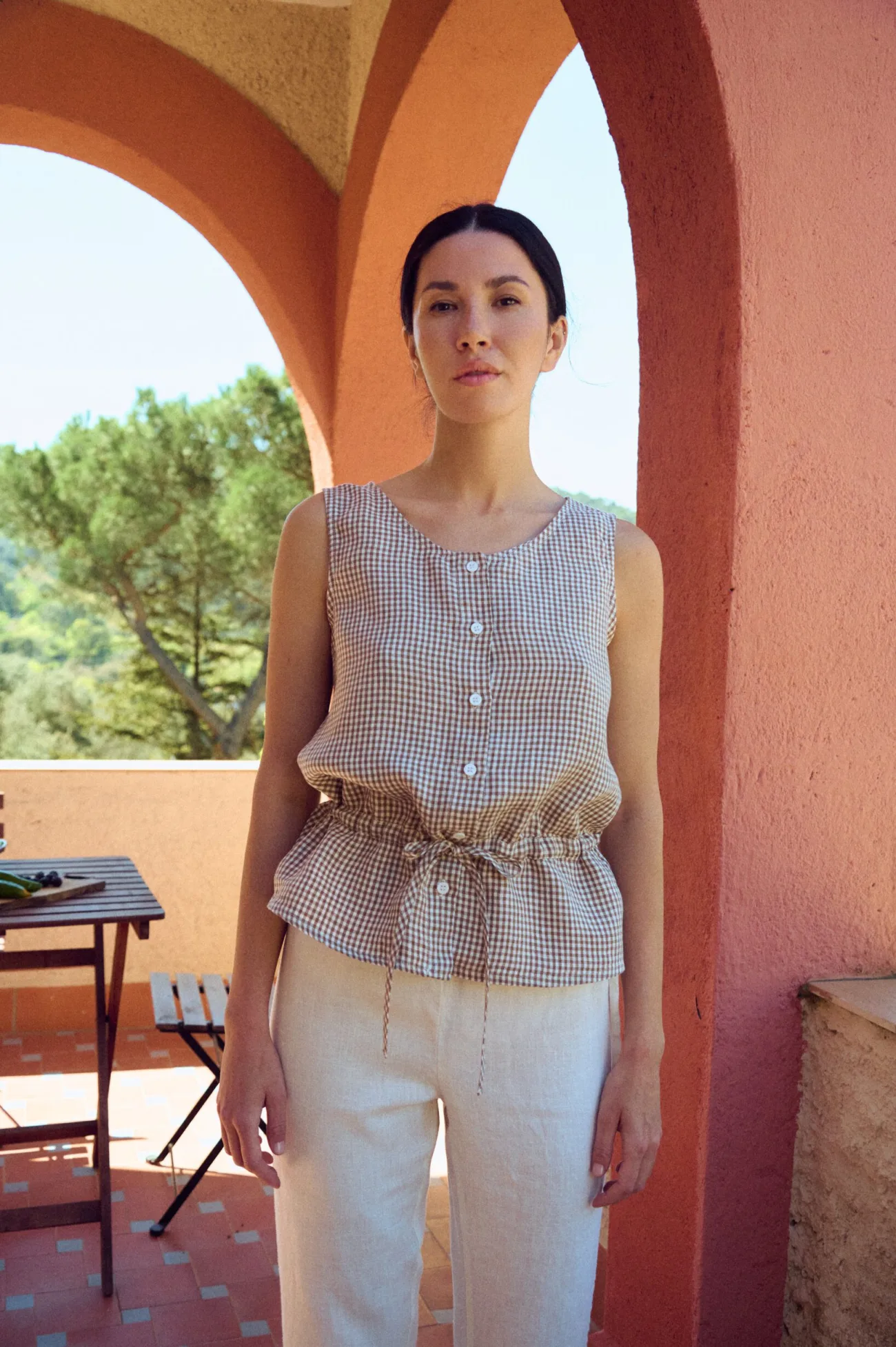 woman wearing brown gingham sleeveless peplum top with drawstring waist and buttons