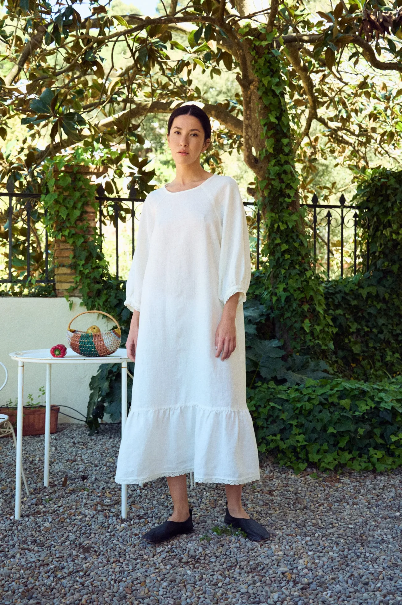 Relaxed white linen dress with a loose, airy silhouette, featuring a soft round neckline, three-quarter sleeves with subtle lace-trimmed cuffs, and a gathered hem panel finished with delicate lace detailing
