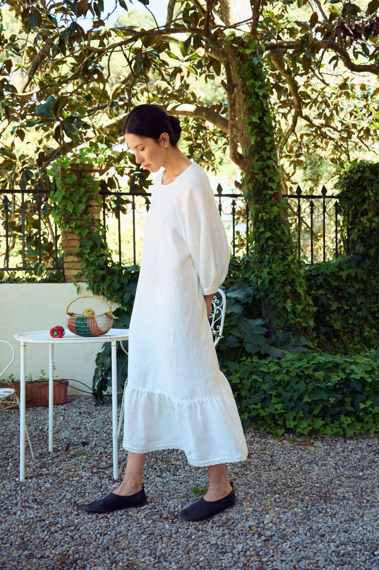 Flowy, mid-length white linen dress with a relaxed silhouette, featuring a clean round neckline, softly gathered three-quarter sleeves, and a tiered hem finished with delicate lace trim