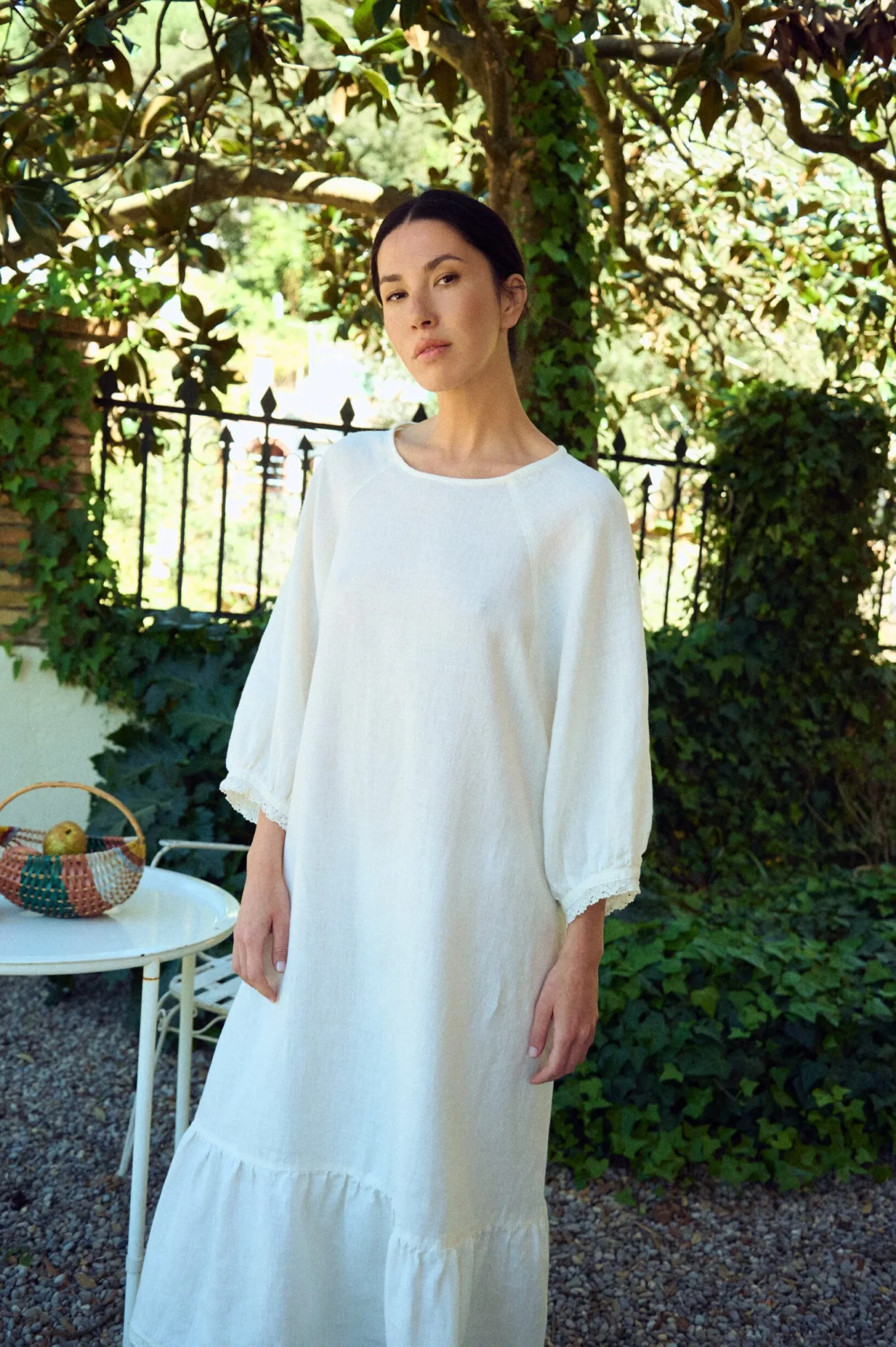 Relaxed white linen dress with a soft, flowing silhouette, featuring a clean round neckline, gently voluminous three-quarter sleeves with lace-trimmed cuffs, and a subtly gathered hem panel