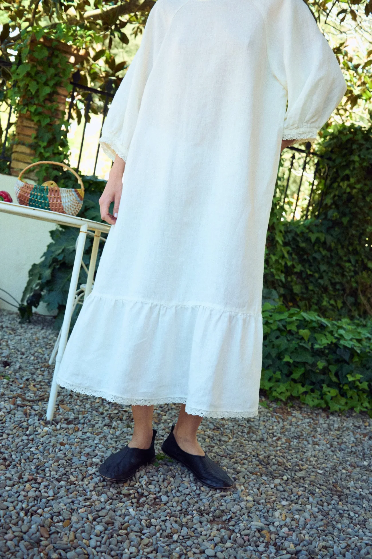 White linen dress with a relaxed, straight silhouette, featuring a softly gathered lower panel and a delicate lace-trimmed hem, complemented by airy three-quarter sleeves with subtle lace detailing