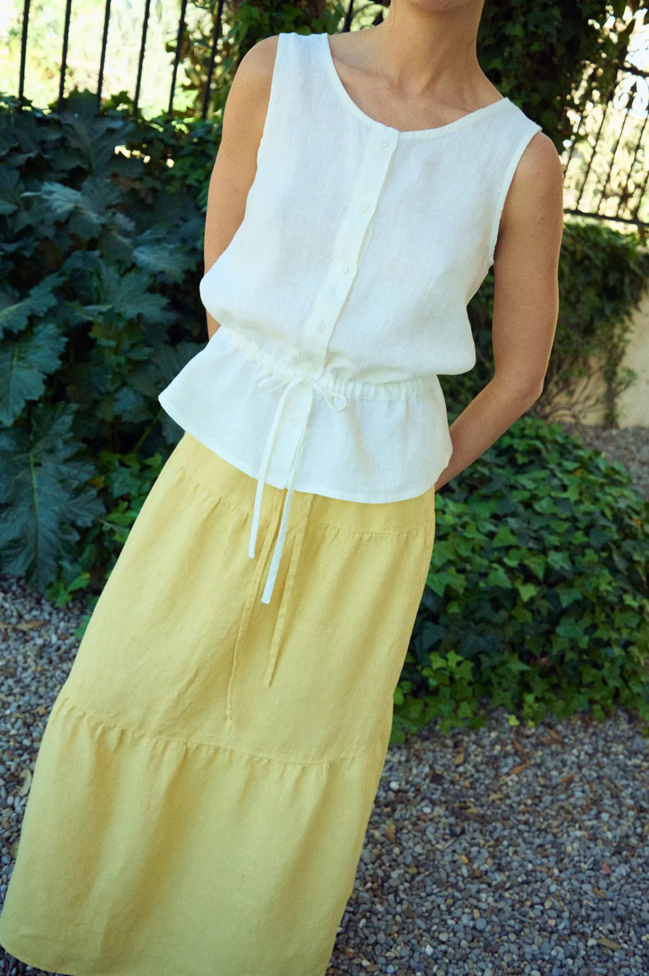 close up of white blouse with round neckline, no sleeves, and tie waist in white linen