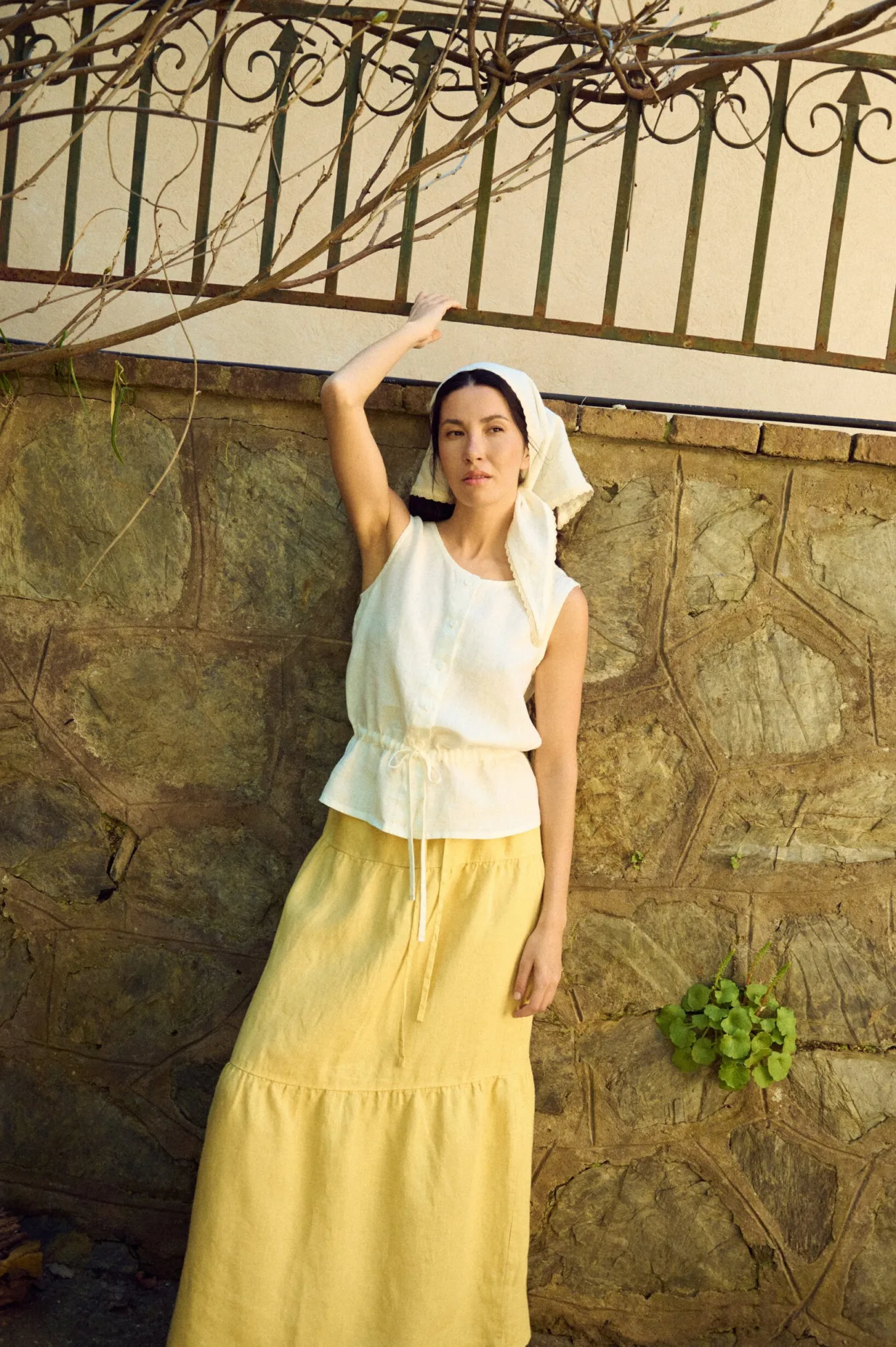 model posing with sleeveless white linen blouse with round neckline and drawstring waist paired with butter yellow skirt
