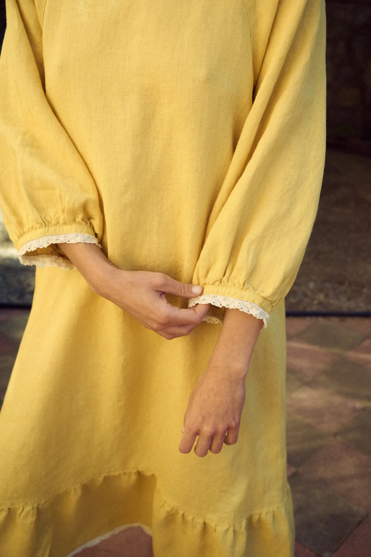 Butter yellow linen dress with a relaxed fit, round neckline, voluminous gathered sleeves with lace-trimmed cuffs, and a tiered hem finished with delicate lace edging