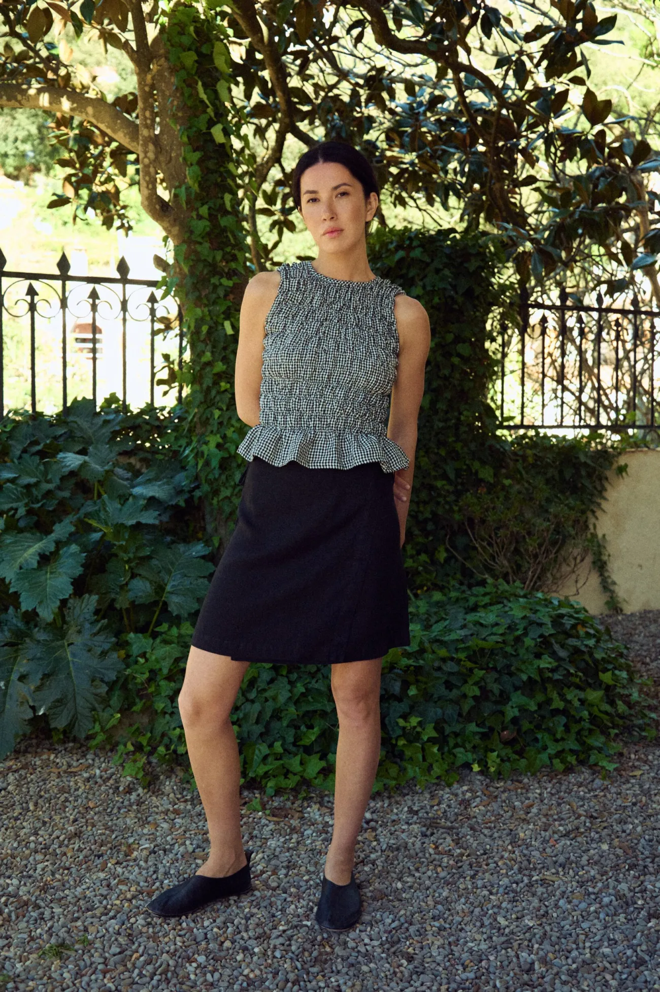 woman wearing black gingham smocked top with flared hem paired with black linen tie waist mini skirt