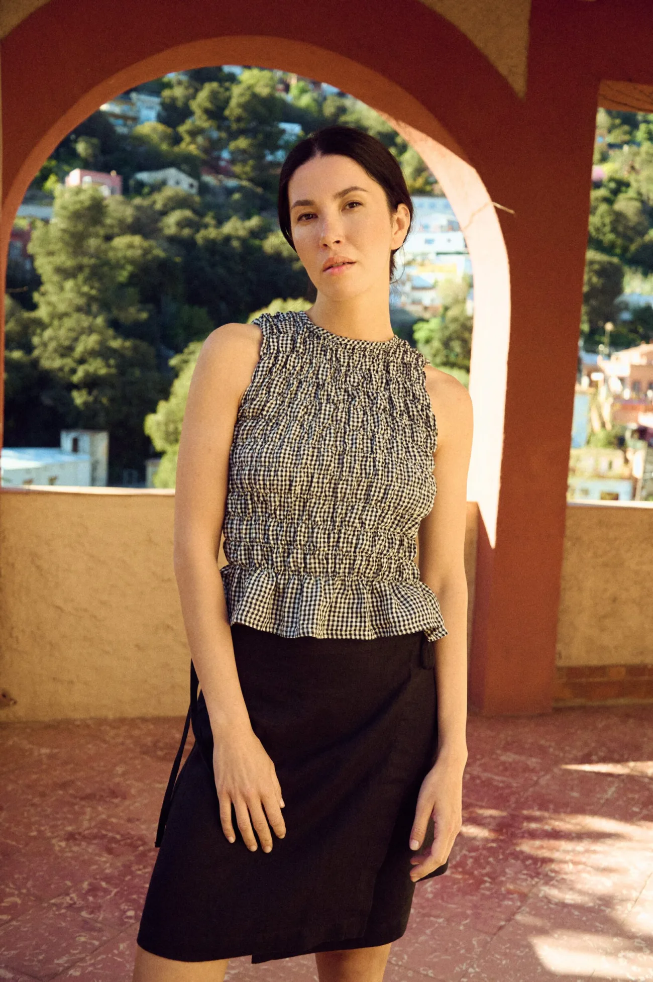 woman posing with smocked black gingham linen top with fitted bodice styled with linen mini skirt in black