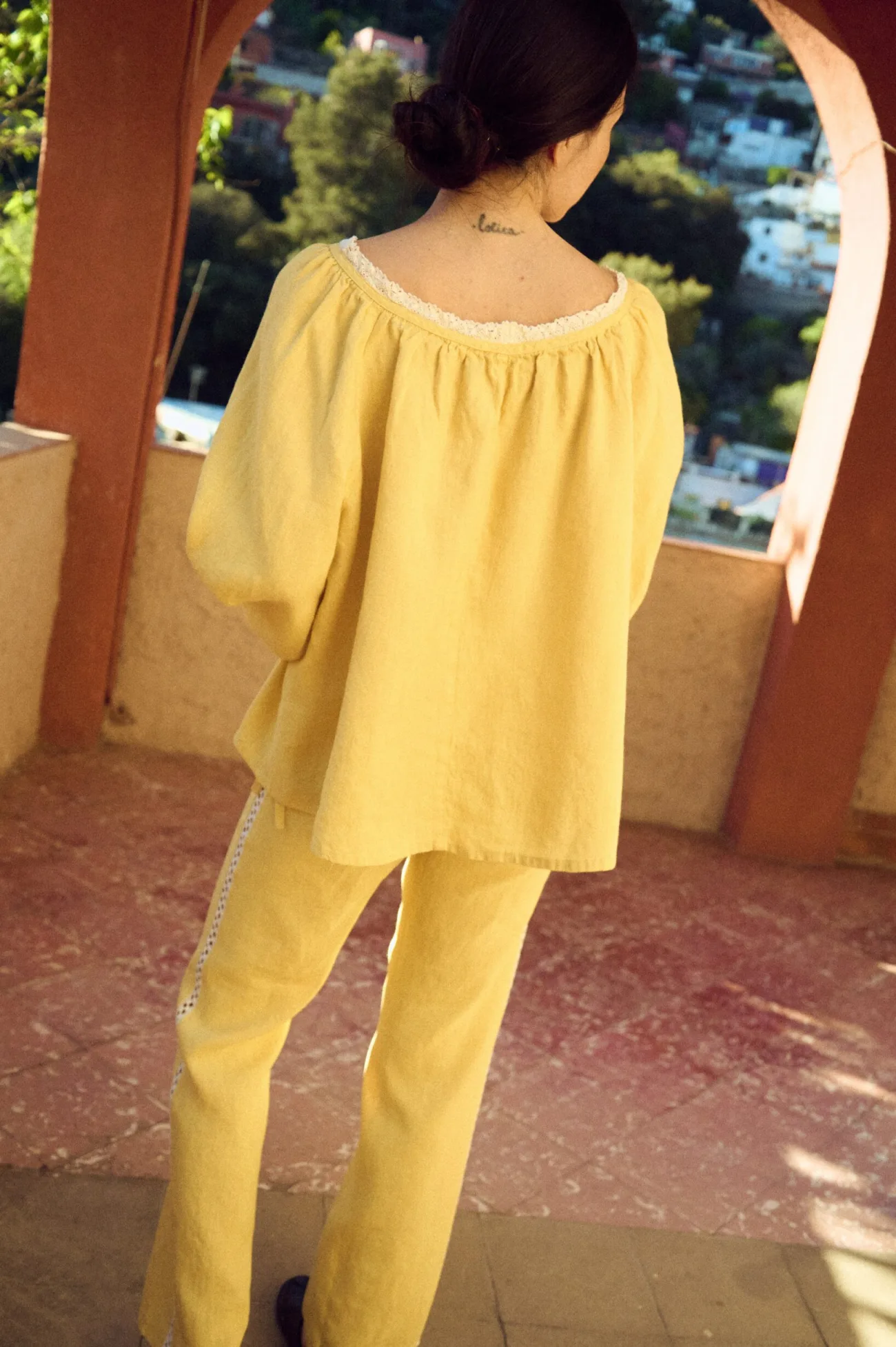 Back view of butter yellow linen blouse with lace-trimmed neckline, soft gathered yoke, and relaxed, airy drape