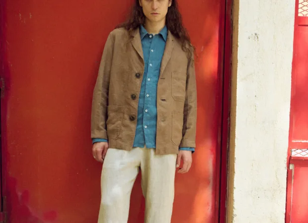 Men’s brown heavy linen jacket with a relaxed blazer-inspired fit, notched lapels, three-button front and roomy patch pockets, layered over a stellar blue linen shirt and loose natural grey linen trousers