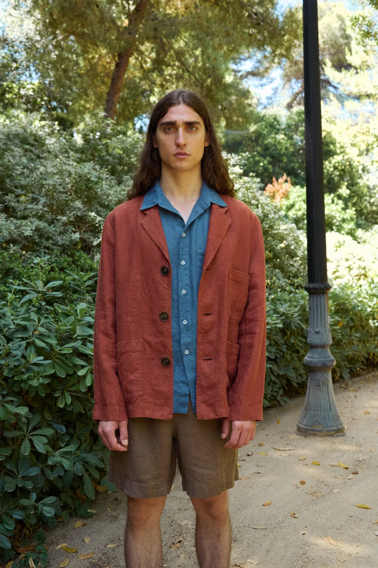 Men’s terracotta heavy linen jacket with a laid-back tailored silhouette, notched lapels, three-button fastening and roomy patch pockets, worn over a stellar blue linen shirt and paired with relaxed brown linen shorts