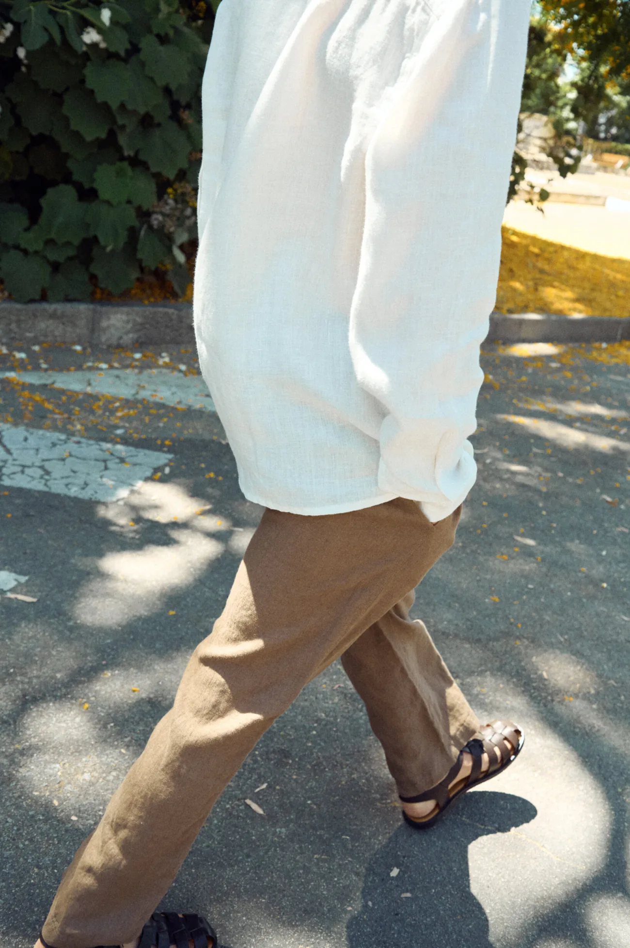 Men’s brown linen trousers with a relaxed straight leg, shown in motion and styled with a white linen shirt