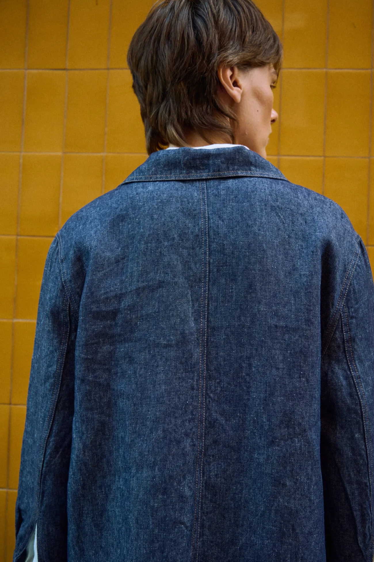 Back detail of blue denim linen jacket showing the center back seam and contrast stitching