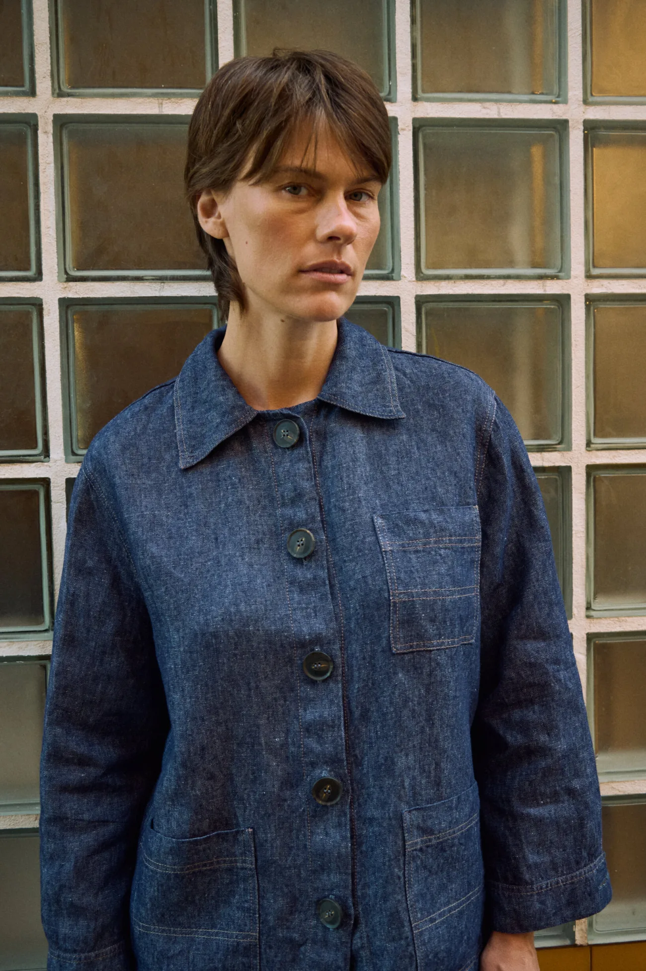 Close-up of blue denim linen jacket with oversized buttons, patch pockets, pointed collar, and contrast stitching