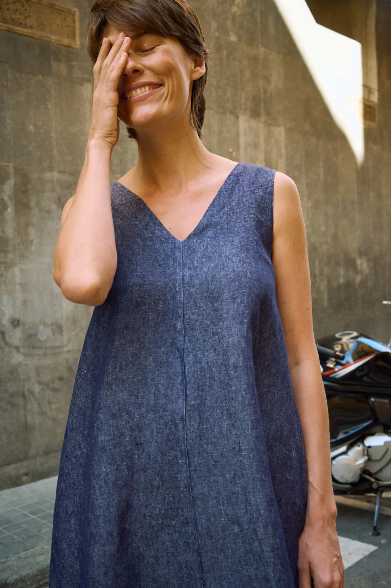 Close-up of a sleeveless blue denim linen maxi dress with a V-neckline, relaxed A-line silhouette and visible center seam