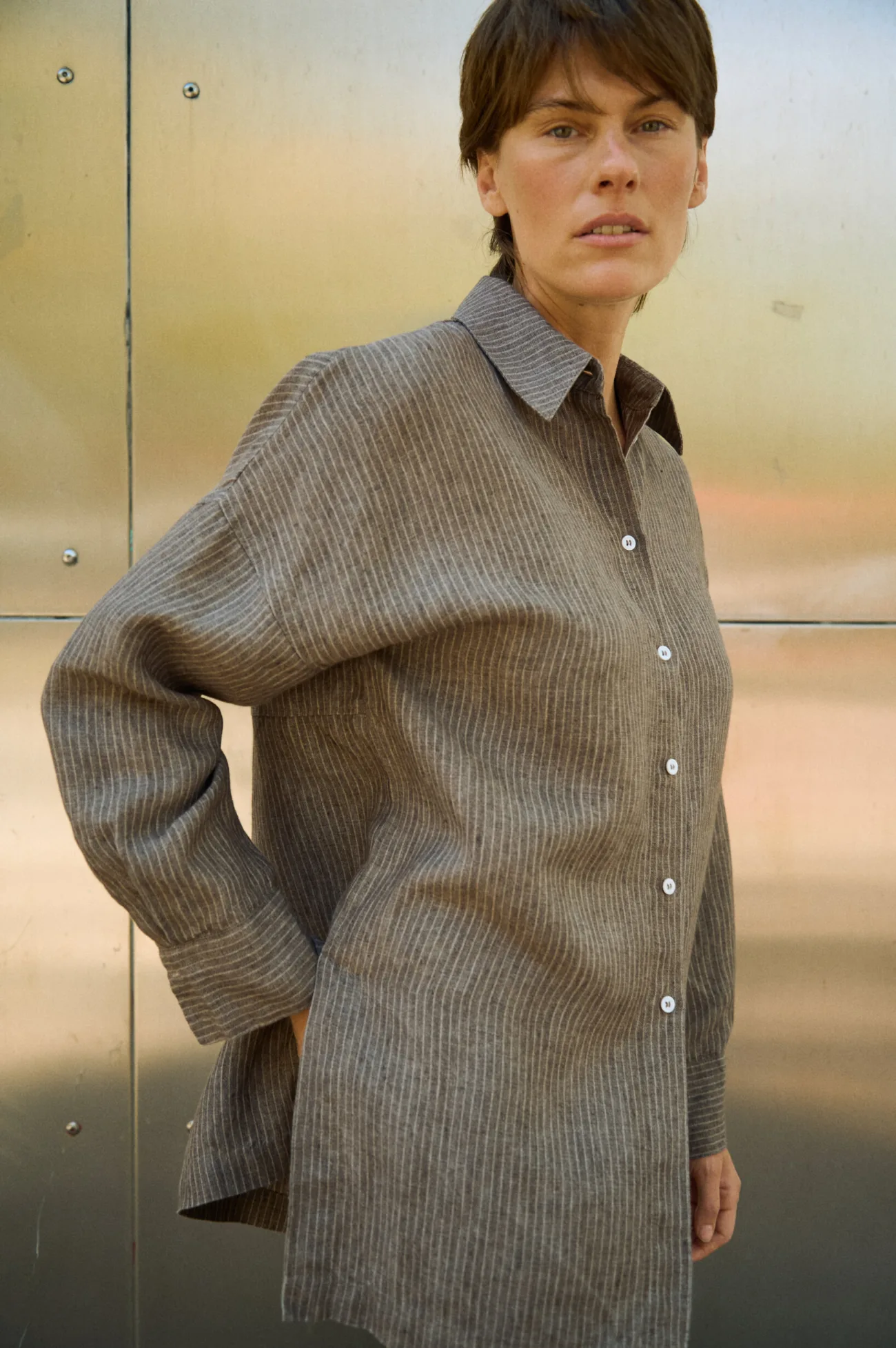 Brown striped linen button-up shirt with a relaxed oversized fit, pointed collar, white buttons and wide cuffs