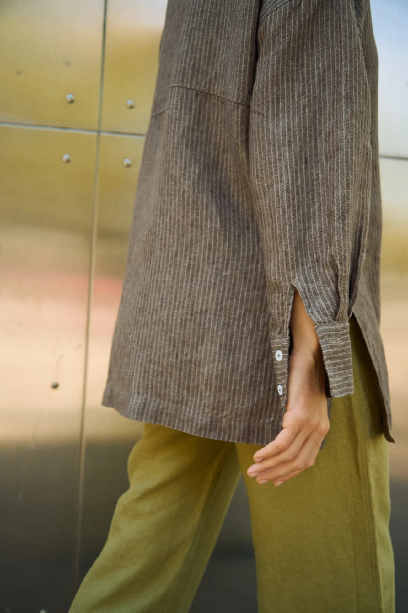 Close-up of a brown striped linen shirt showing the side slit, long hem and buttoned cuff detail