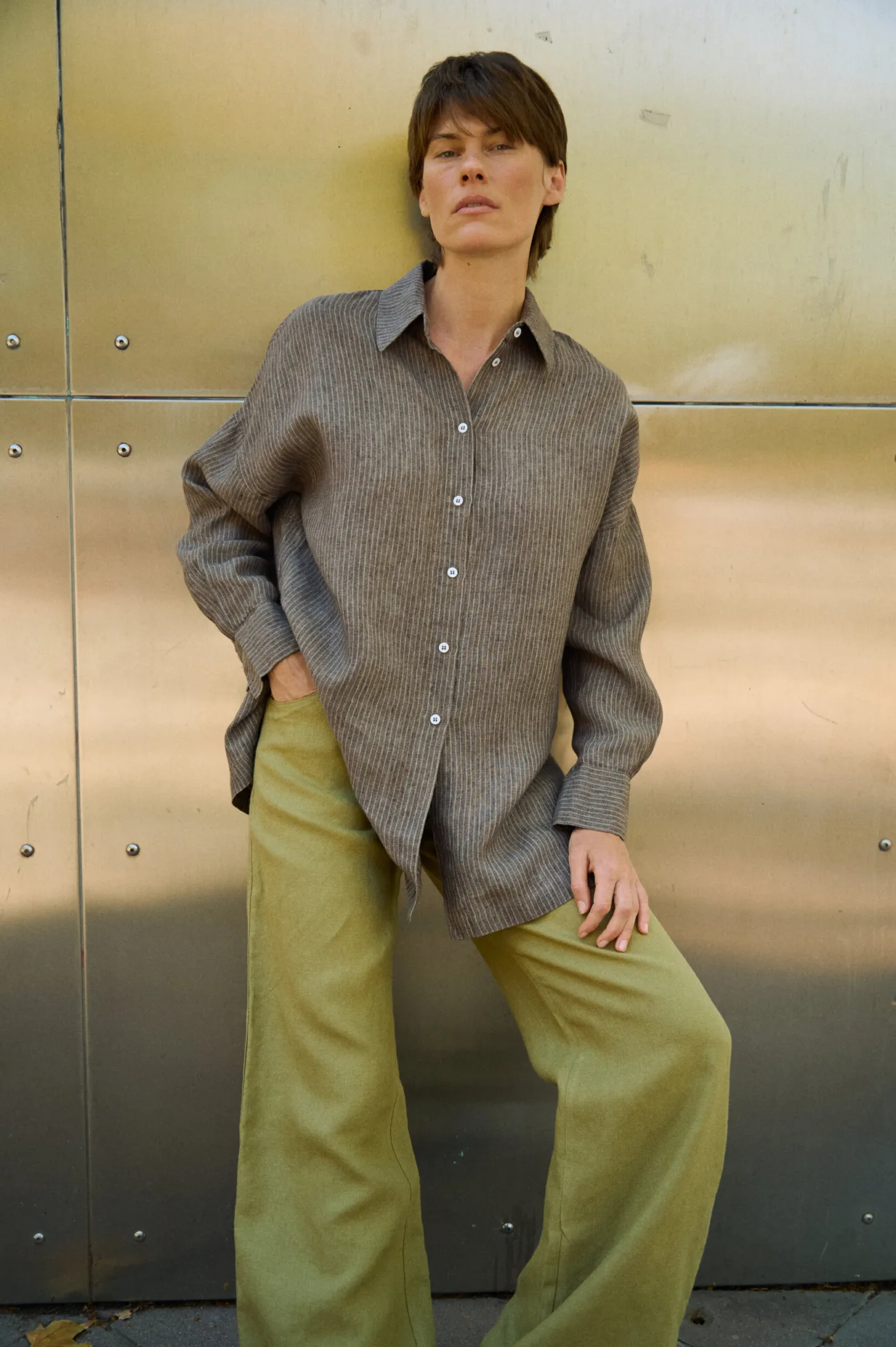 Brown striped linen button-up shirt with a loose draped fit, styled with olive green wide-leg trousers