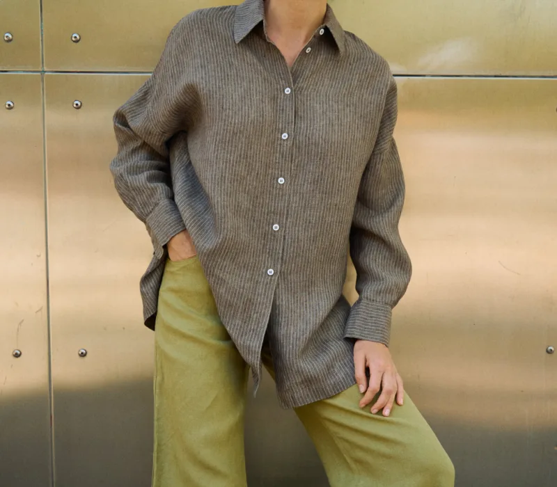 Brown striped linen button-up shirt with a loose draped fit, styled with olive green wide-leg trousers