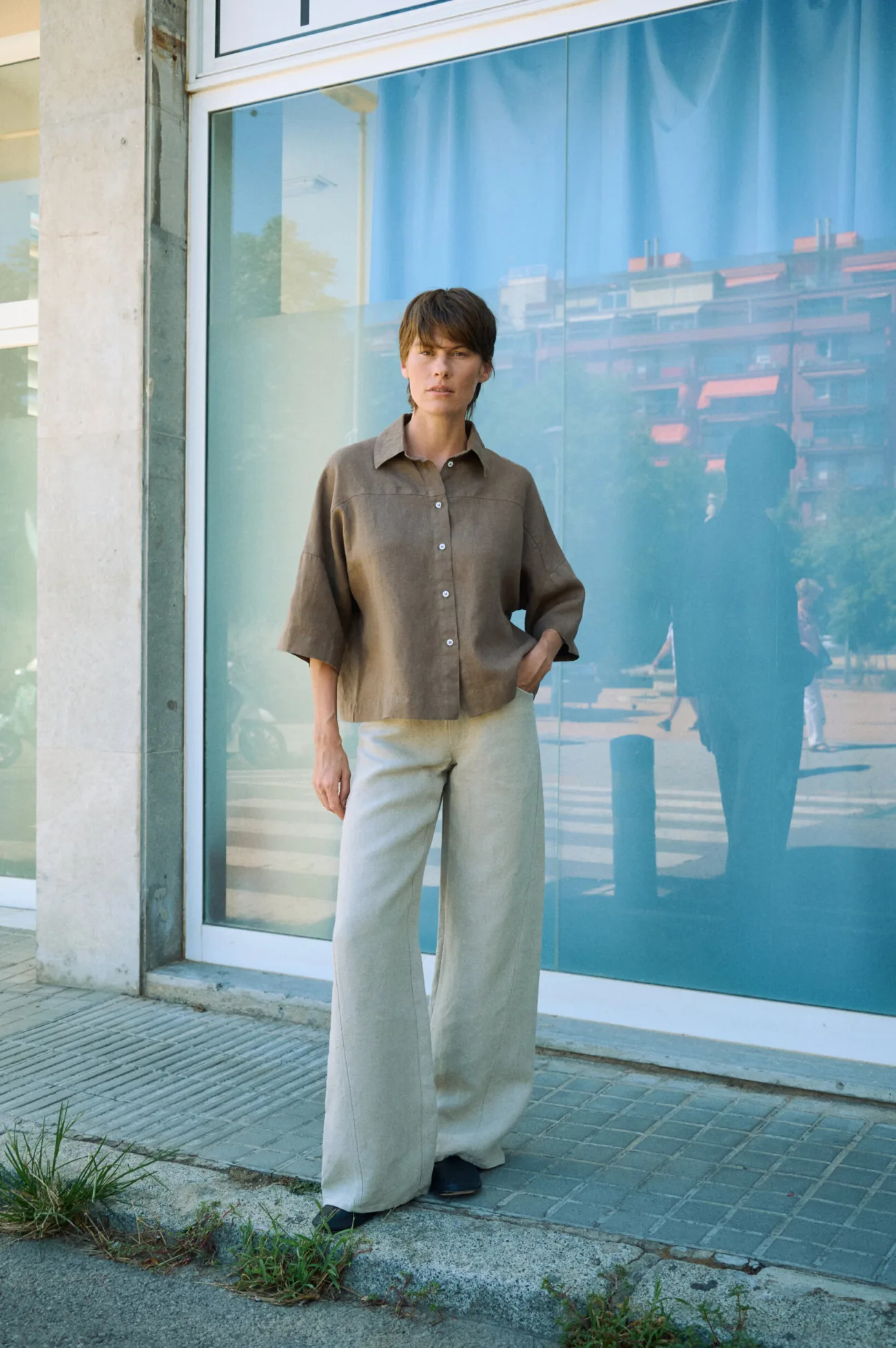 Natural grey heavy linen wide-leg trousers with a relaxed full-length silhouette, styled with a brown linen button-up shirt