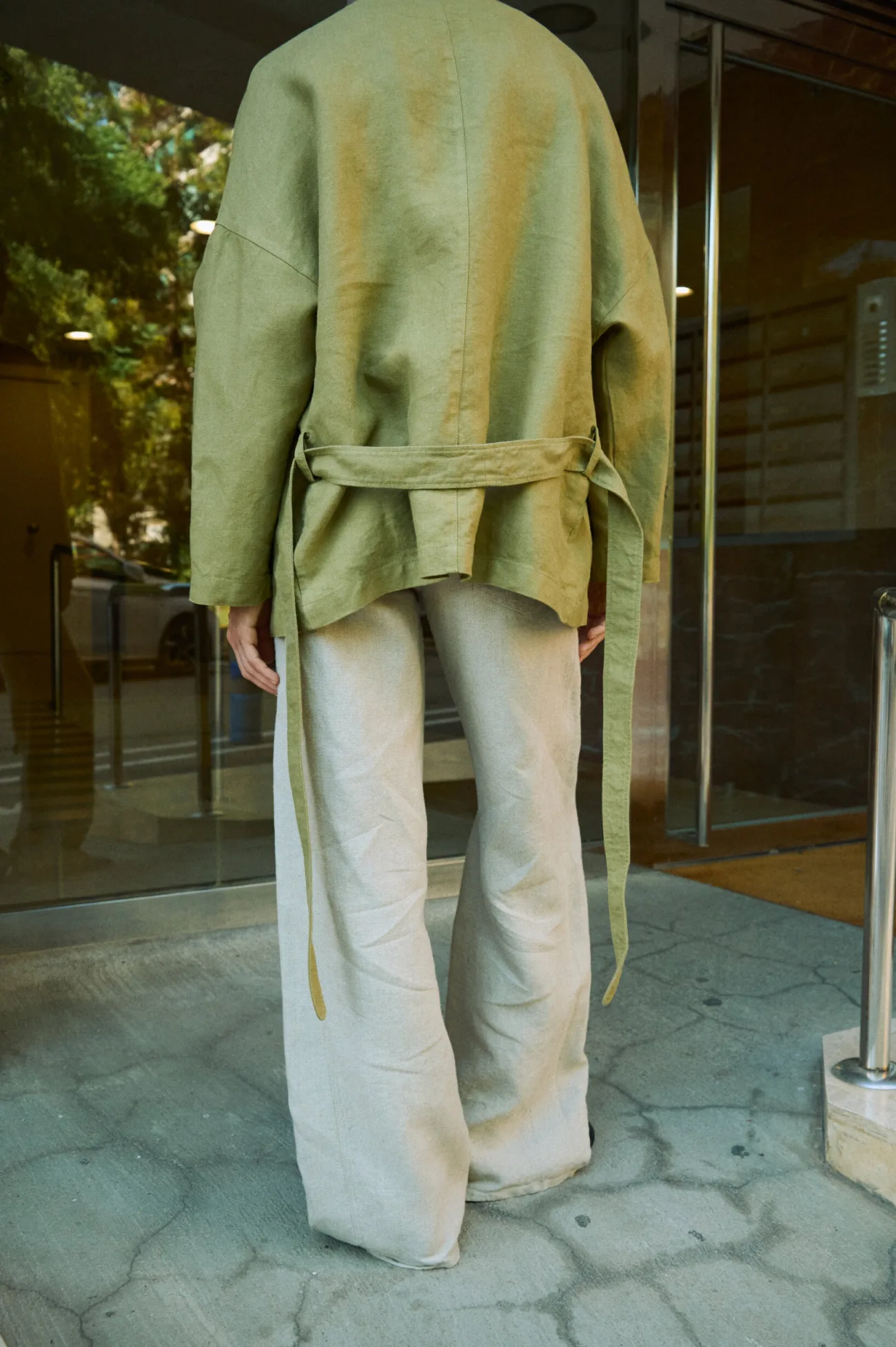 Rear view of natural grey heavy linen wide-leg trousers styled with an olive green linen tie jacket