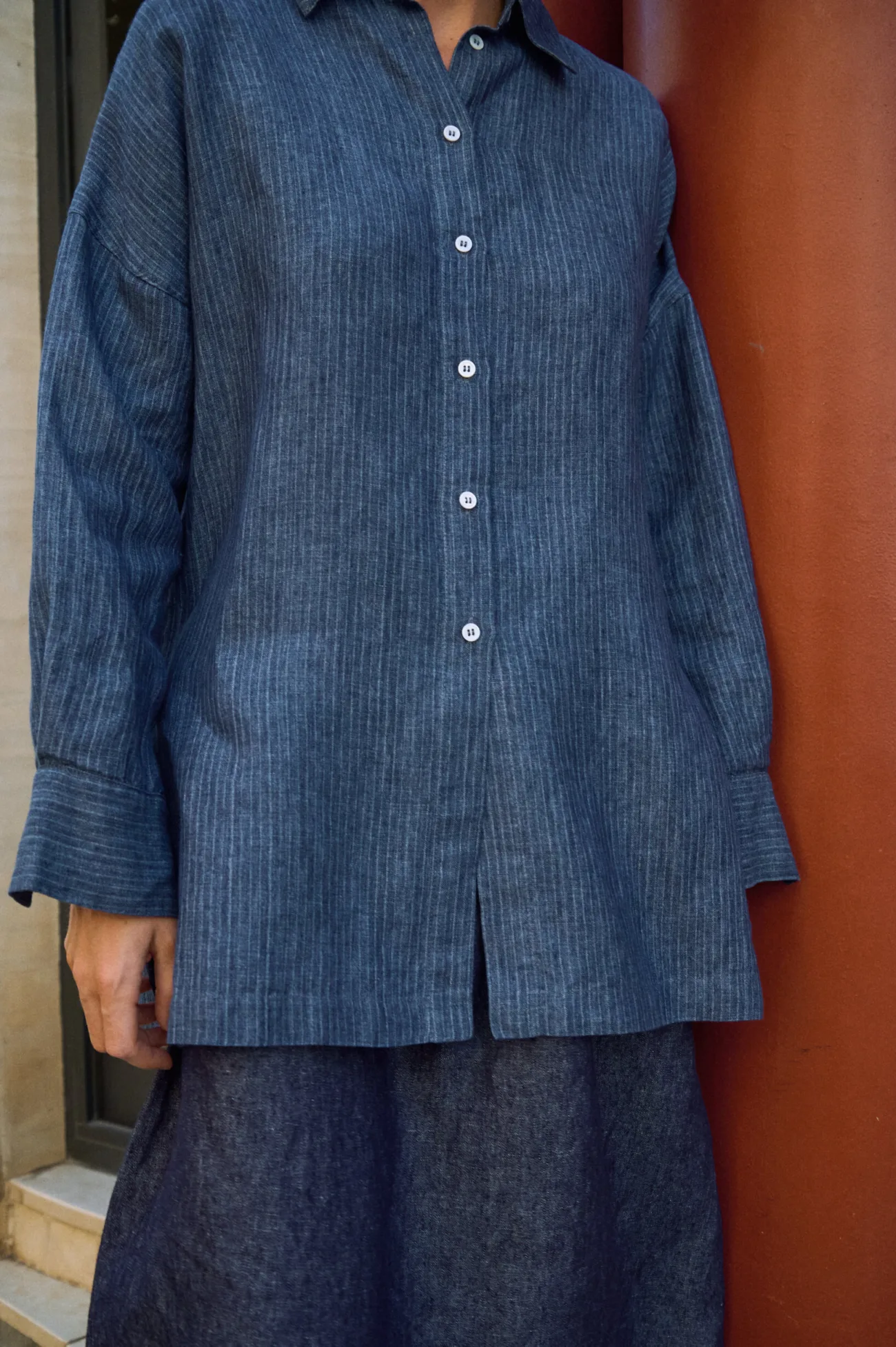 Close-up of a blue striped linen button-up shirt with white buttons, dropped shoulders and wide cuffs