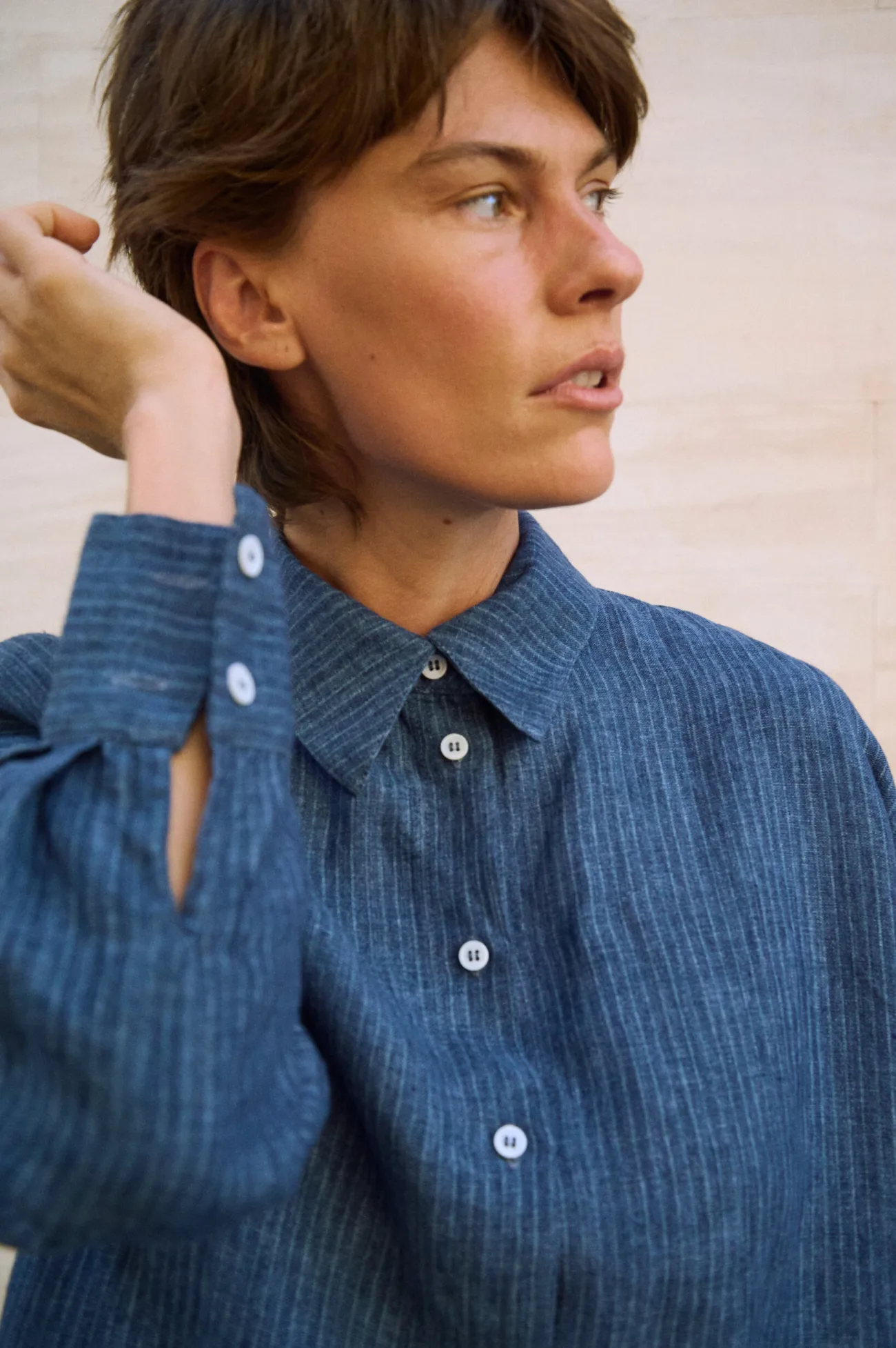 Close-up of a blue striped linen button-up shirt showing the pointed collar, white buttons and wide buttoned cuffs