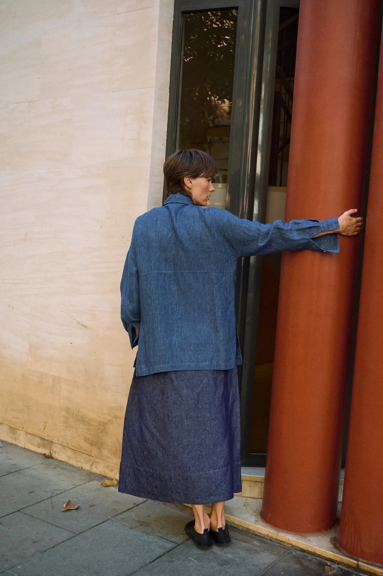 Rear view of a denim linen maxi skirt with a gently flared shape, paired with an oversized blue striped linen shirt