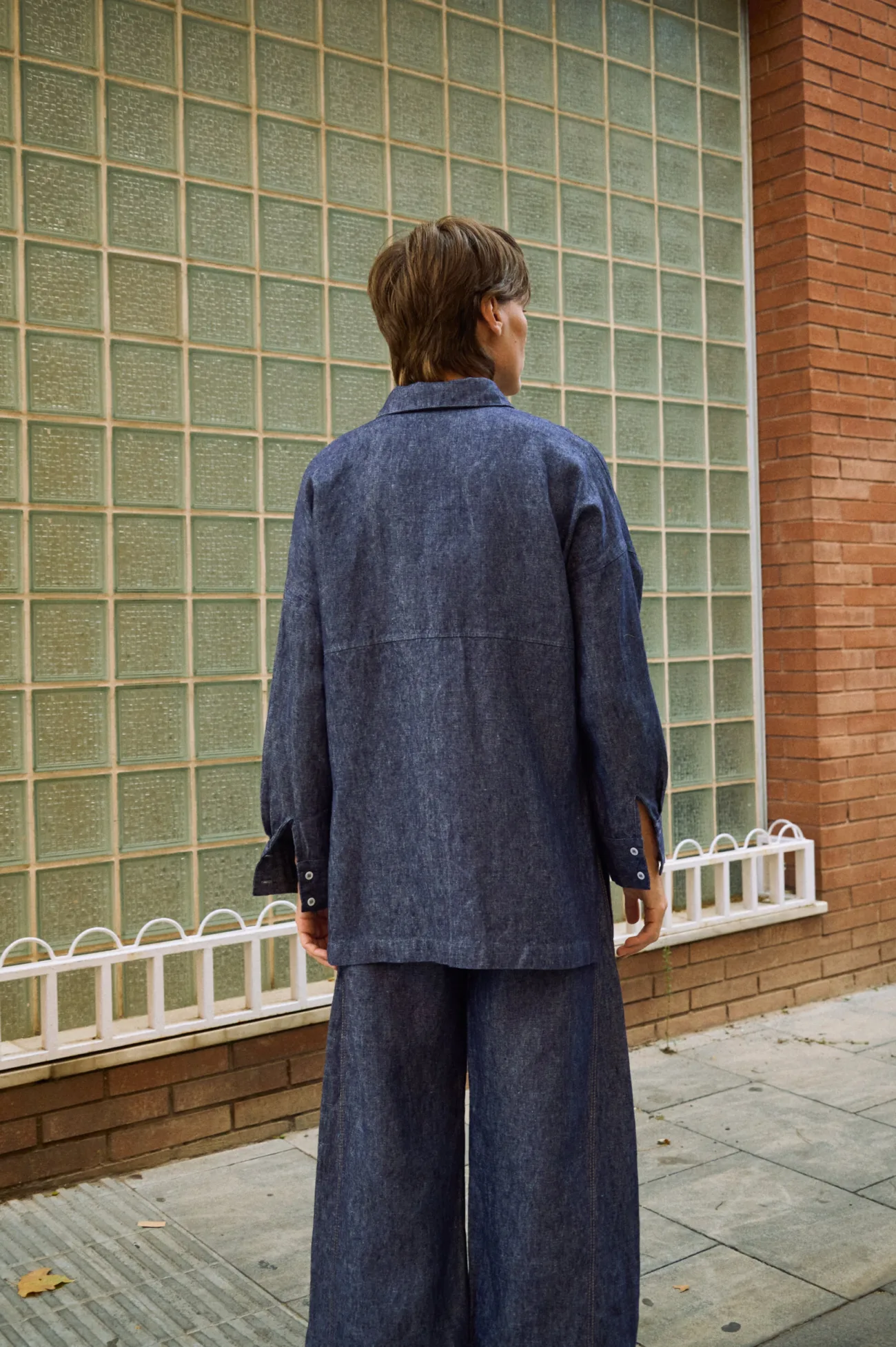 Back view of blue denim linen shirt with relaxed fit, dropped shoulders, and buttoned cuffs