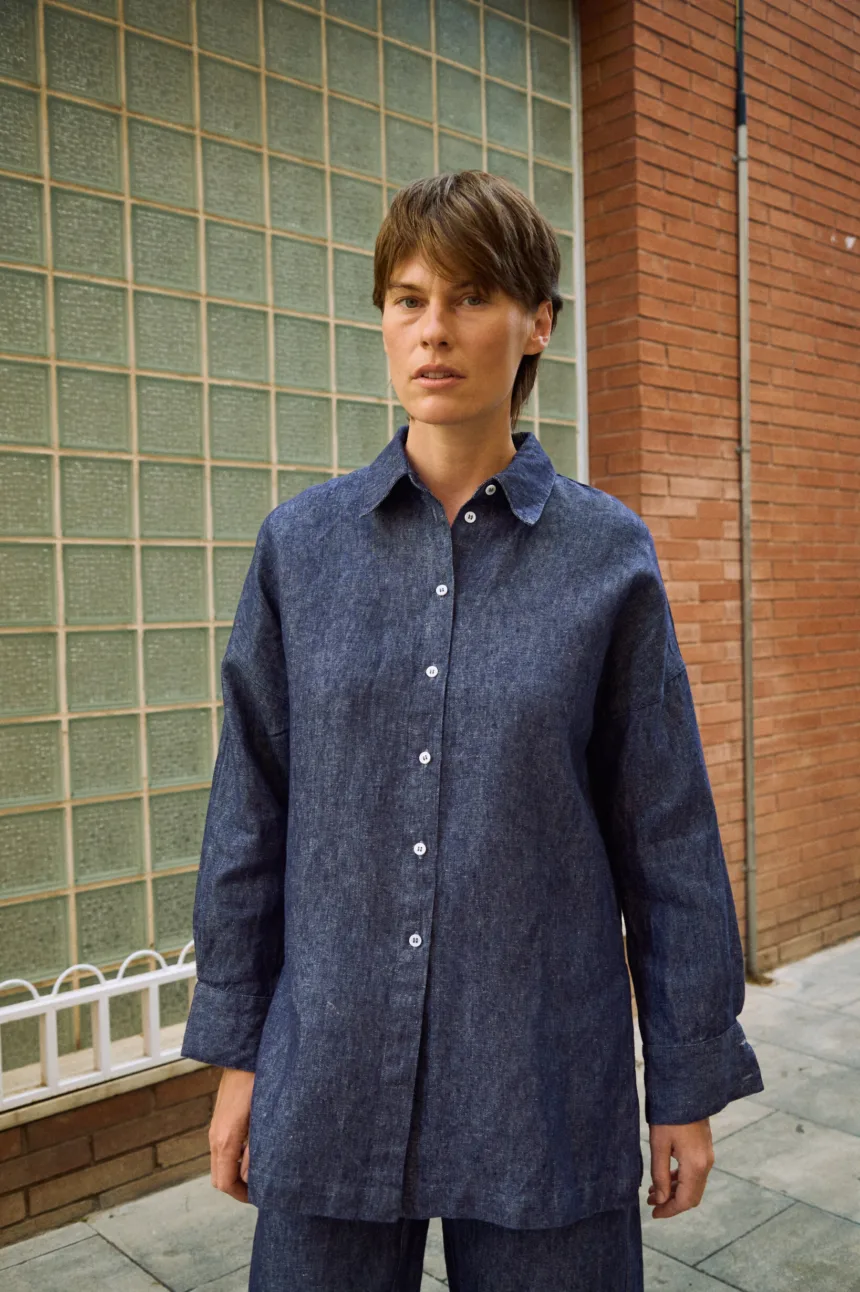 Front detail of blue denim linen shirt with button-down front, pointed collar, dropped shoulders, and wide cuffs